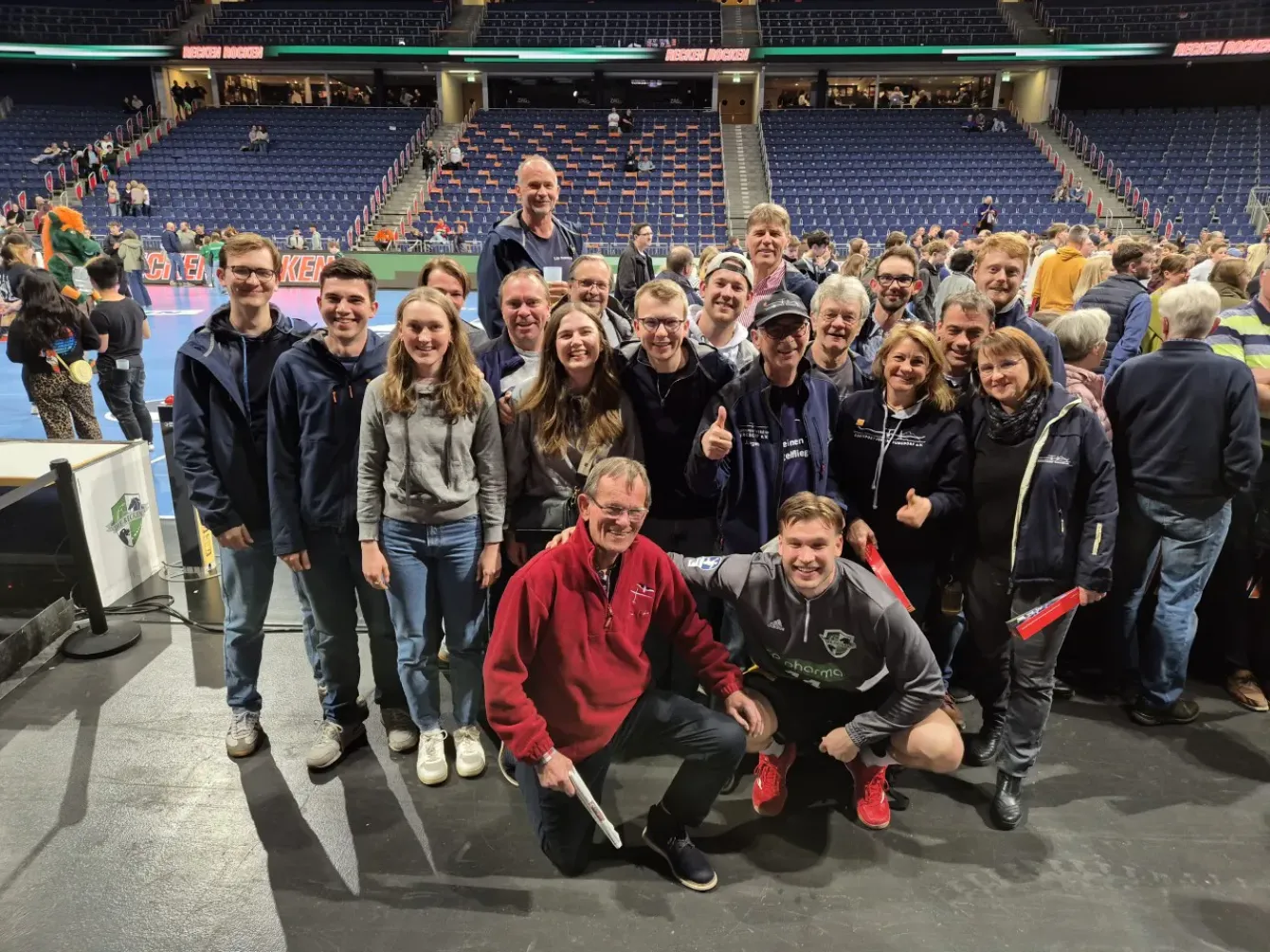 Gruppe von Menschen posiert lächelnd in einer Sportarena.