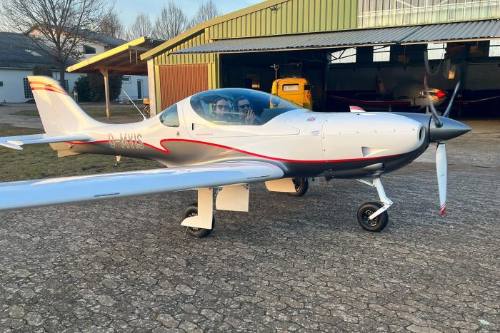 Weißes Kleinflugzeug vor einem Hangar auf einem Flugplatz.